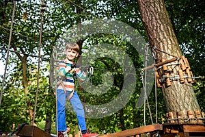 Happy kid playing at adventure park, holding ropes and climbing wooden stairs