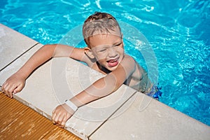 Happy kid playing in blue water of swimming pool.