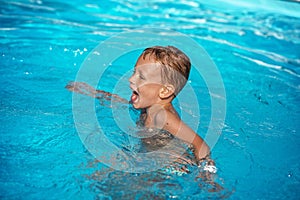 Happy kid playing in blue water of swimming pool.