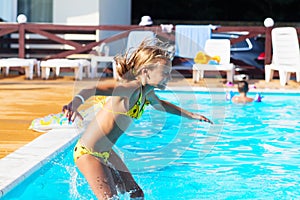 Happy kid playing in blue water of swimming pool. Little girl le