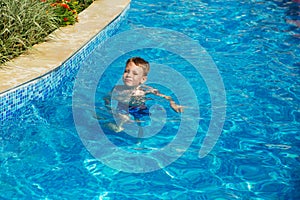 Happy kid playing in blue water of swimming pool on a tropical r