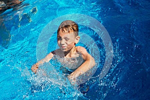 Happy kid playing in blue water of swimming pool on a tropical r