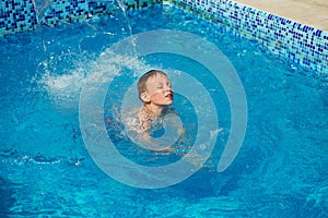 Happy kid playing in blue water of swimming pool on a tropical r