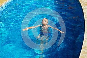 Happy kid playing in blue water of swimming pool on a tropical r