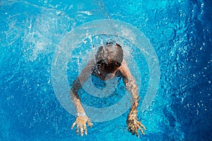 Happy kid playing in blue water of swimming pool on a tropical r