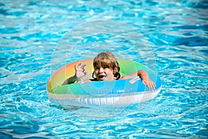 Happy kid playing with colorful swim ring in swimming pool on summer day. Child water toys. Children play in tropical