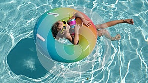 Happy kid playing with colorful swim ring in swimming pool on summer day. Child water toys. Children play in tropical