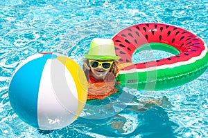 Happy kid playing with colorful swim ring in swimming pool on summer day. Child water vacation. Children play in