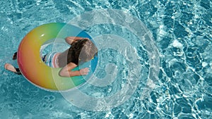 Happy kid playing with colorful swim ring in swimming pool on summer day. Children playing in the swimming pool. Summer