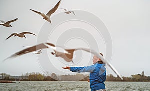 Happy kid is playing and feeding seagulls in summer beach. School child boy chasing birds in the sea beach in Poole