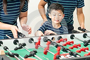 Happy kid playing foosball table with family.