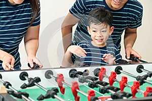 Happy kid playing foosball table with family.