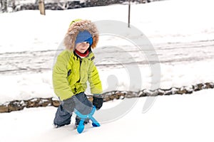 Happy kid plays with snow. Little boy in fashion winter outfit outdoors. Family winter vacation