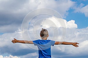 Happy kid with raised arms against blue sky. Freedom, joy and happiness concept