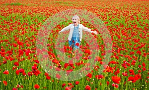 Happy kid resting on a beautiful poppy field. Child having fun outdoor. Little girl playing in field with red poppies