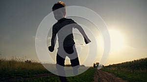 Happy kid run along rural road. Child run along road along wheat field. Happy child is playing at sunset. Silhouette of