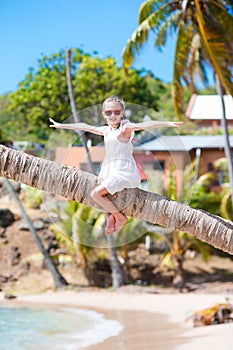 Happy kid sitting on palm tree during caribbean vacation on white beach