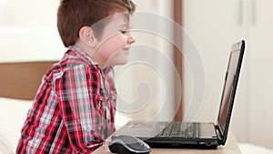 Happy kid skyping via laptop, smiling child at home, little boy watching funny cartoons at gadget