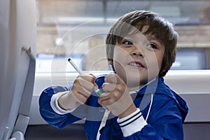 Happy kid with smiling face holding colour pen sitting next to window of the train, Child boy travelling to to school by the high