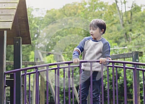 Happy kid standing on bridge on tree house in playground Active child wearing jumper playing outdoor in forest park, Portrair