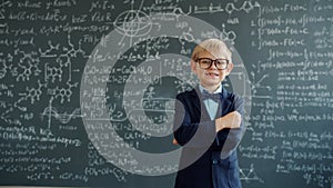 Happy kid in suit and glasses standing in class with chalkboard in background