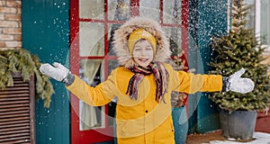 Happy kid throws snow overhead on the background of Christmas tree and lights. Smiling boy having fun outdoors, on the decorated