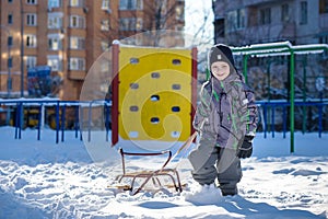 Happy kid walking outdoors in winter city drags his sled. child smiling and having fun.