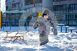 Happy kid walking outdoors in winter city drags his sled. child smiling and having fun.