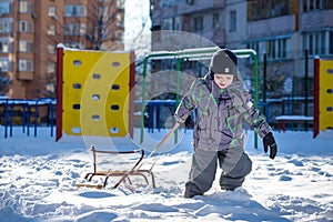 Happy kid walking outdoors in winter city drags his sled. child smiling and having fun.