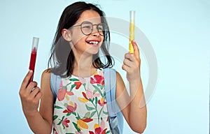 Happy kid wearing floral dress and eyeglasses with blue backpack smiling and looking at her new markers. A child has joyful