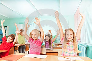 Happy kids with arms up sit in classroom rows