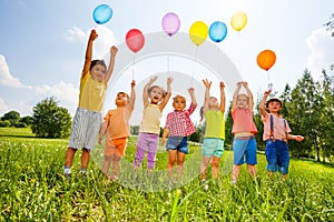 Happy kids with balloons and arms up in the sky