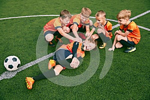 Happy kids, beginner soccer players having rest after sports training at sports stadium, outdoors. Concept of sport