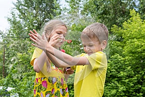 Happy kids boy and girl have fun in the park blowing rainbow bubbles and catching and popping them