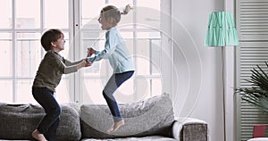 Happy kids boy and girl having fun jumping on sofa