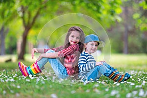Happy kids boy and girl in rain rubber boots playing outside in the green park with blooming field of daisy flowers