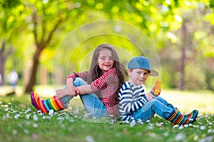 Happy kids boy and girl in rain rubber boots playing outside in the green park with blooming field of daisy flowers