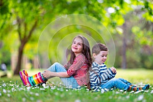 Happy kids boy and girl in rain rubber boots playing outside in the green park with blooming field of daisy flowers