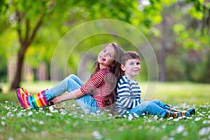 Happy kids boy and girl in rain rubber boots playing outside in the green park with blooming field of daisy flowers