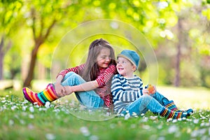 Happy kids boy and girl in rain rubber boots playing outside in the green park with blooming field of daisy flowers