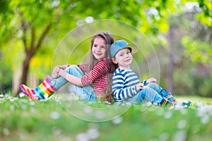 Happy kids boy and girl in rain rubber boots playing outside in the green park with blooming field of daisy flowers