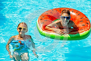 Happy kids, boy and girl in sunglasses, swim and play with inflatable rings in the pool, have fun during family summer vacation