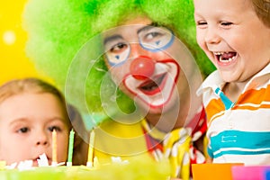 Happy kids and clown blowing candles on cake