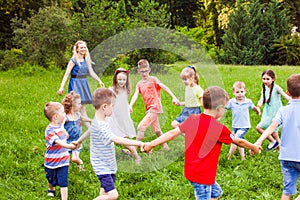 Happy kids dancing in circle on green lawn in park