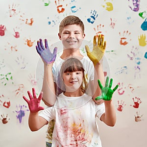 Happy kids, disabled boy and girl with Down syndrome smiling at camera, showing their hands painted in colorful paints