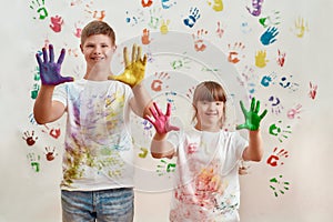 Happy kids, disabled boy and girl with Down syndrome smiling at camera, showing their hands painted in colorful paints