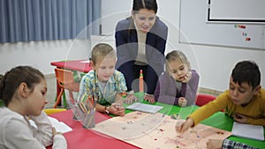 Happy kids and female teacher playing together educational board game in classroom at elementary school