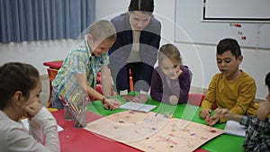 Happy kids and female teacher playing together educational board game in classroom at elementary school