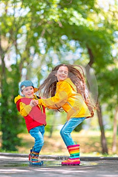 Happy kids girl and boy with umbrella and colorful rubber rain boots playing outdoor and jumping in rainy puddle