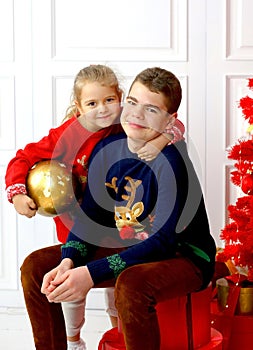 Happy kids girl and teenager, brother and sister smiling in Christmas sweaters playing with a golden ball sitting by the Christmas